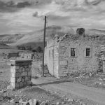 Black and white photo of an abandoned stone house in a barren desert landscape.